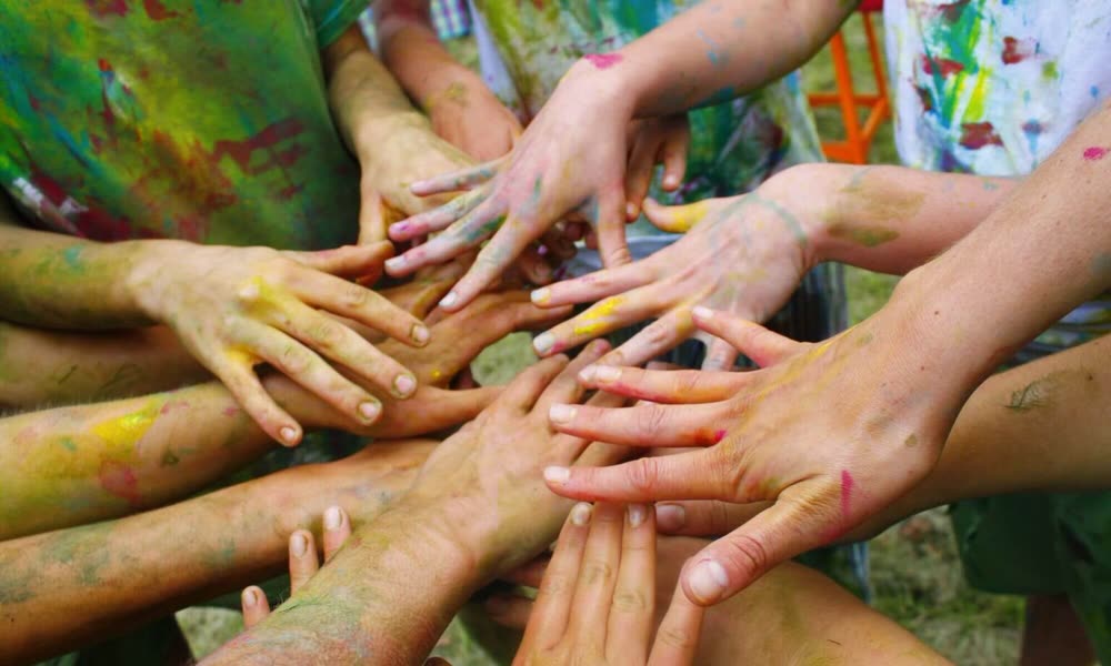 Manos de un grupo de personas unidas, cubiertas de pintura de colores